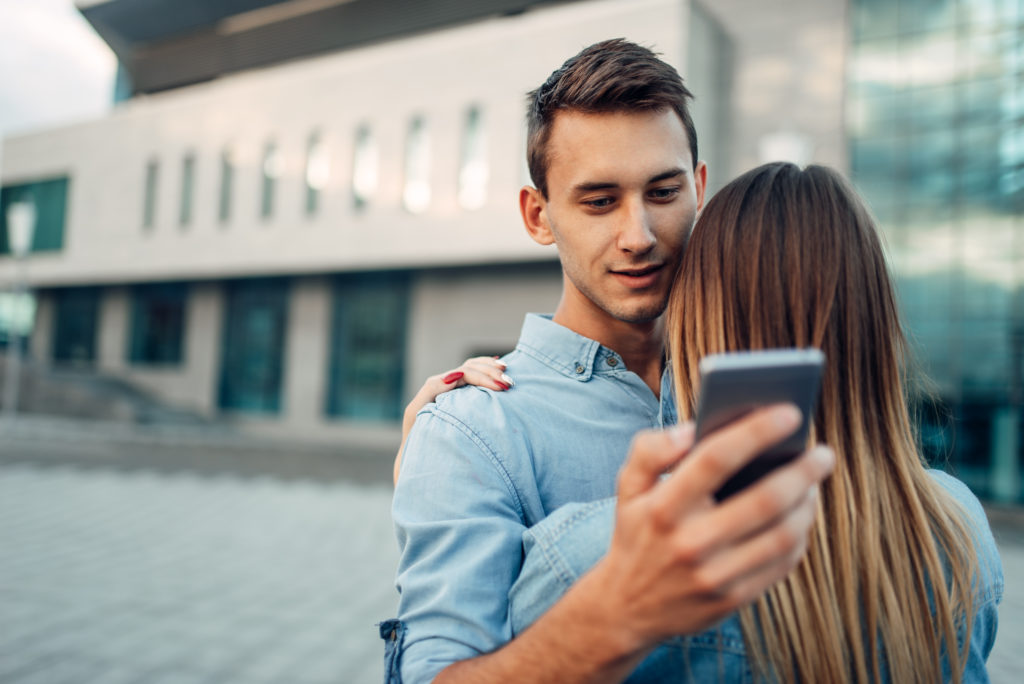 Phone addict man hugs his woman and using gadget